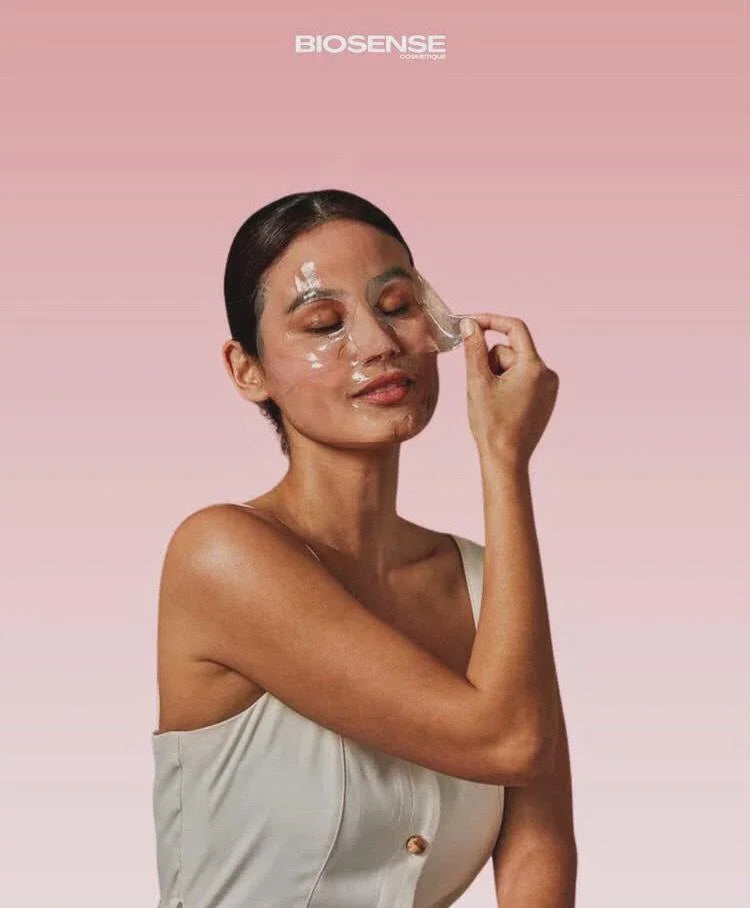 Woman peeling off clear facial mask on pink background, showcasing skincare treatment by Biosense